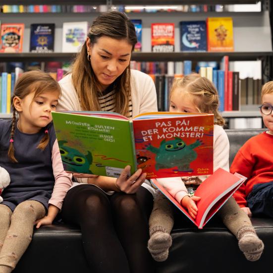 Foto af bibliotekar med billedbog og børn omkring
