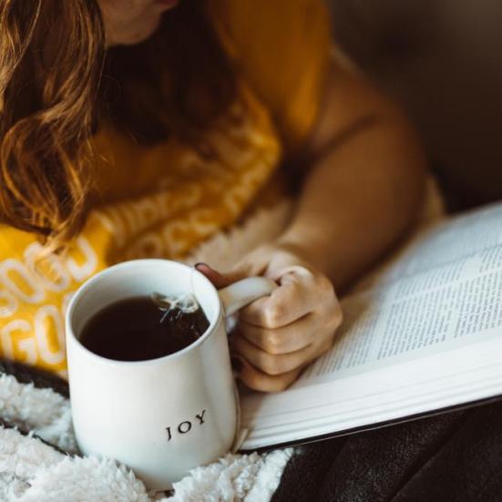 Læsende kvinde med en kop kaffe i hånden
