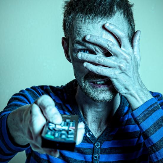 En mand ser fjernsyn, men holder sig for øjnene.