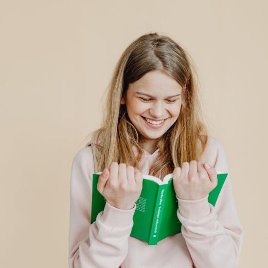 Smilende ung person holder og læser en grøn bog tæt ind til sig og smiler.