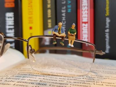 Et par briller der ligger på et bord med to små mennesker på brillekanten