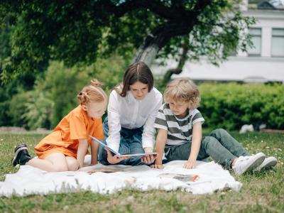 En mor læser højt for to børn udendørs