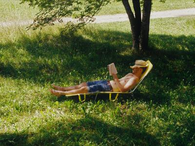 Mand der ligger i skyggen af et træ og læser en bog