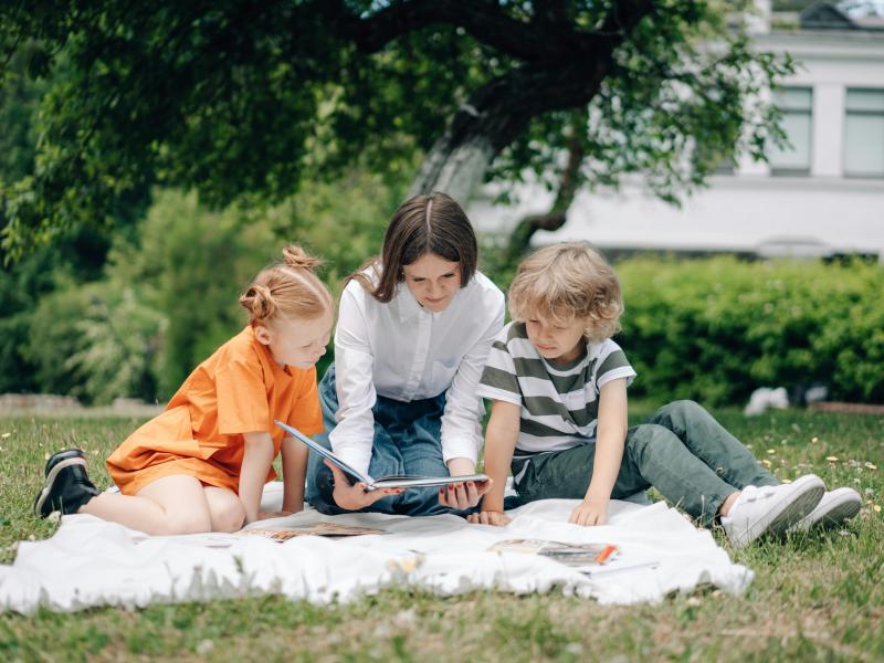 En mor læser højt for to børn udendørs