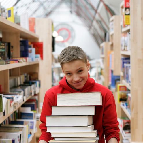 Dreng står på bibliotek med favn fuld af bøger