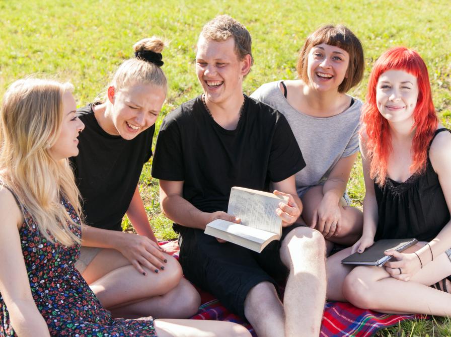 Unge mennesker, der læser og smiler på græsplæne