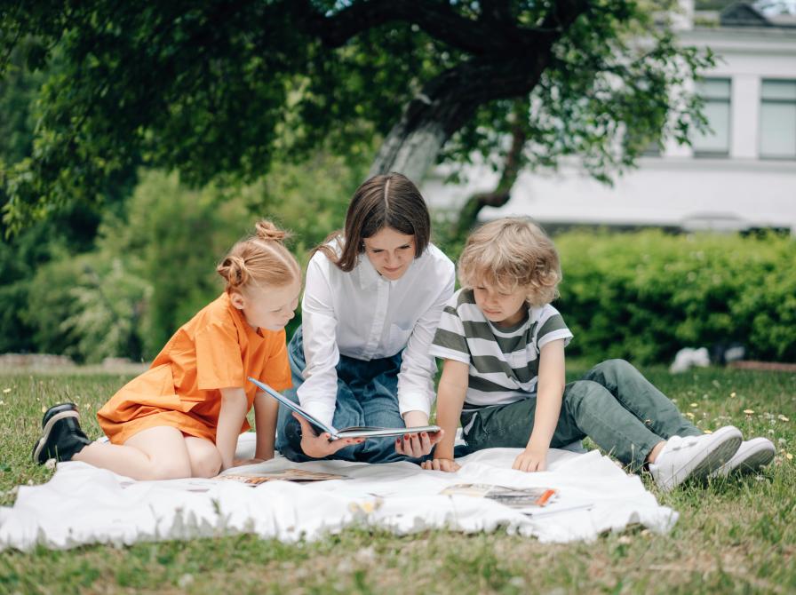 En mor læser højt for to børn udendørs