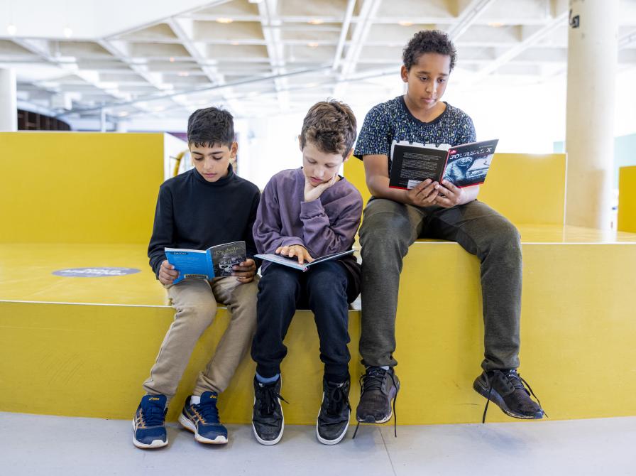 Tre drenge sidder på biblioteket og læser i hver sin bog