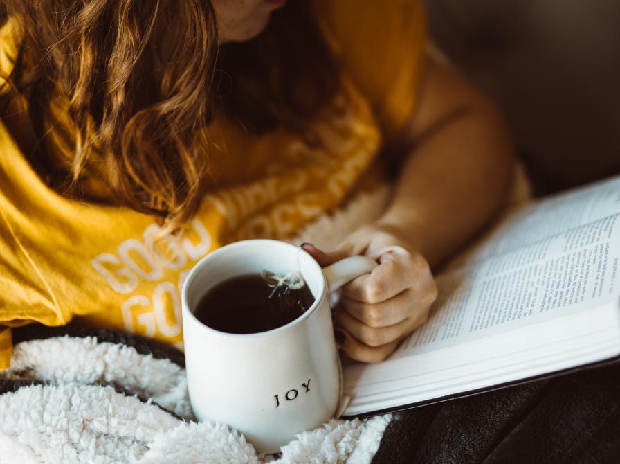 Læsende kvinde med en kop kaffe i hånden