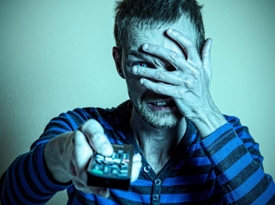 En mand ser fjernsyn, men holder sig for øjnene.